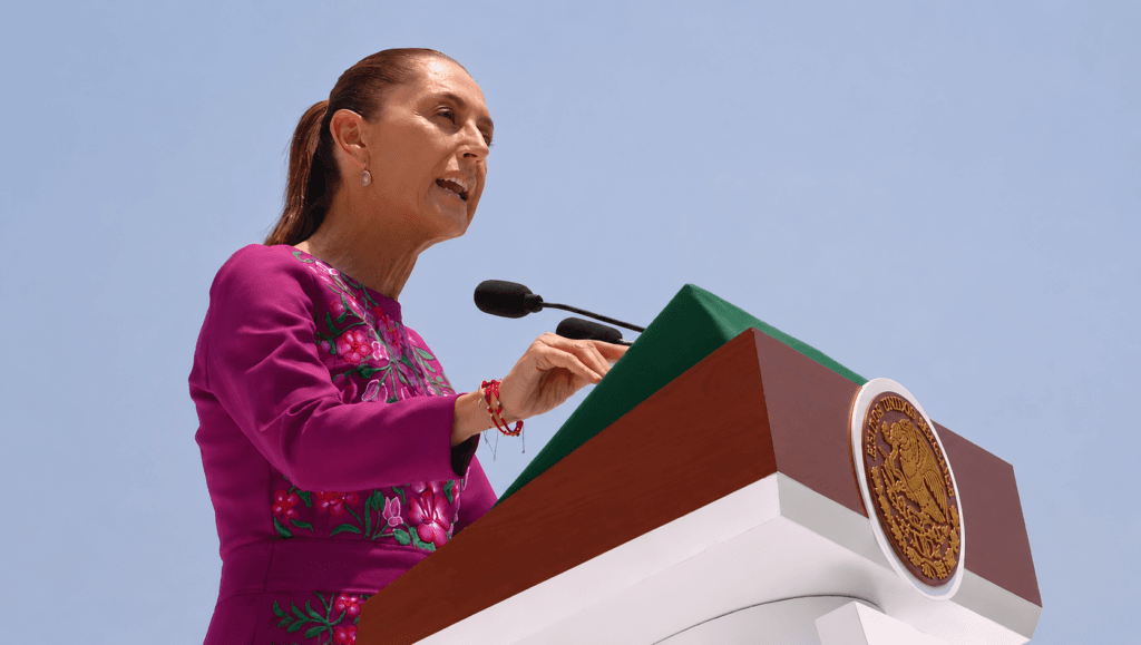 Claudia Sheinbaum, presidenta de México, ofrece un discurso conmemorativo en un podio con el emblema nacional, defendiendo