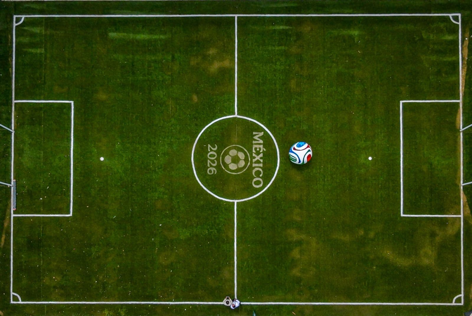 Campo de fútbol con el logo del Mundial 2026 en México, balón en el centro y líneas de juego bien definidas.