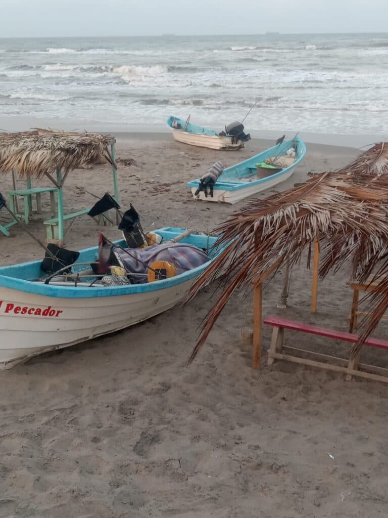 Botes de pesca en la playa de Playa Hermosa, con sombrillas y sillas de palapa, reflejando la actividad turística y las problemáticas locales.