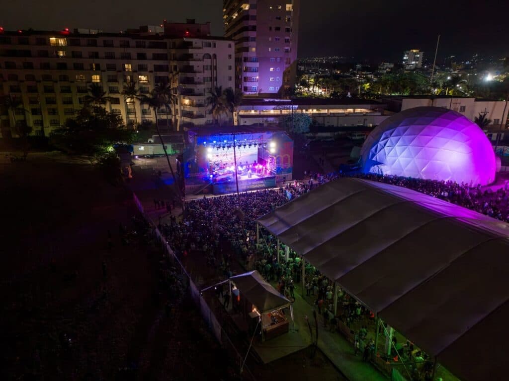 Gran concierto al aire libre en Jalisco con multitudes disfrutando de la música bajo luces coloridas, en un ambiente festivo.