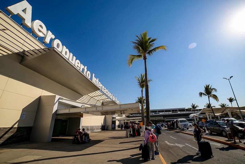 Aeropuerto Internacional de Guadalajara con pasajeros y palmeras, escenario de sorteos de vuelos nacionales en Mundo Jalisco.