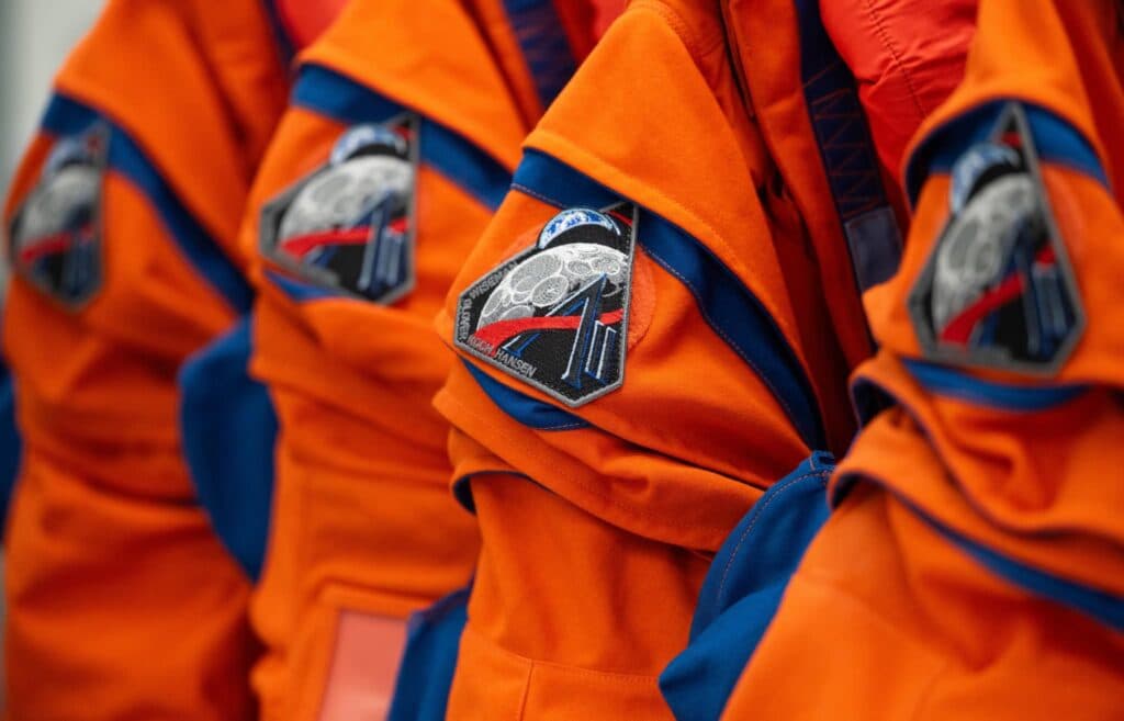 Uniformes de astronautas de la misión Artemis III, con parches que representan el regreso a la Luna y la exploración espacial.