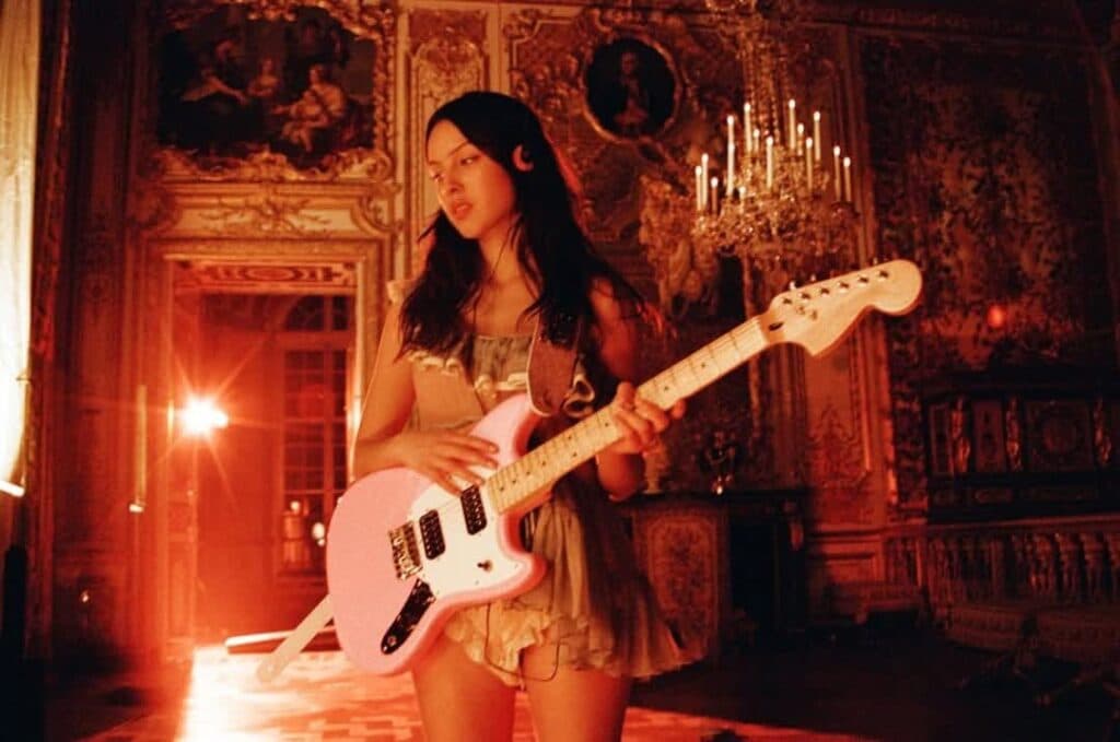 Mujer con guitarra rosa en un entorno elegante y decorado, simbolizando el empoderamiento femenino en la música.
