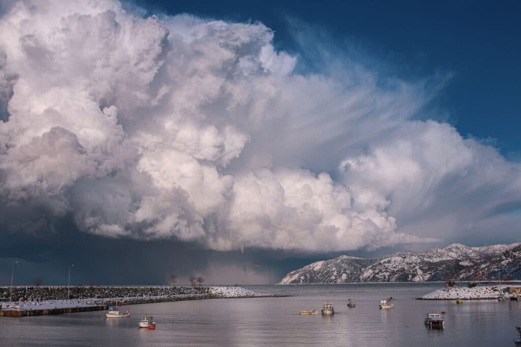 Nubes densas y amenazantes sobre un paisaje costero con barcos en el agua, reflejando condiciones climáticas inestables.