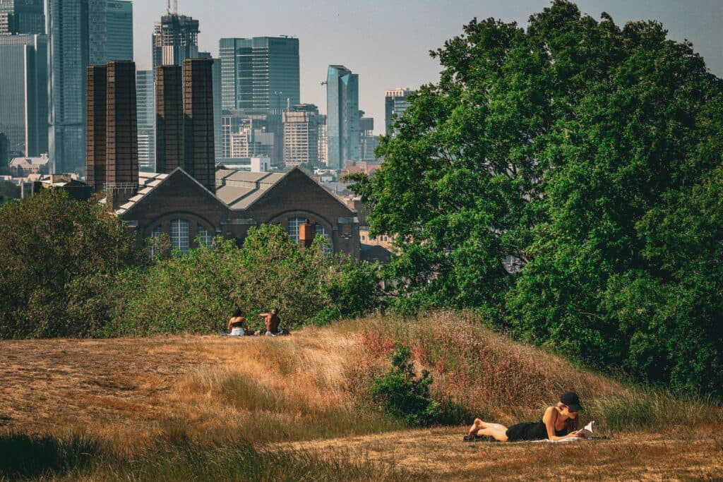 Personas descansando en un área verde de Londres mientras se observa el skyline urbano, reflejando el impacto de la ola de calor extremo.