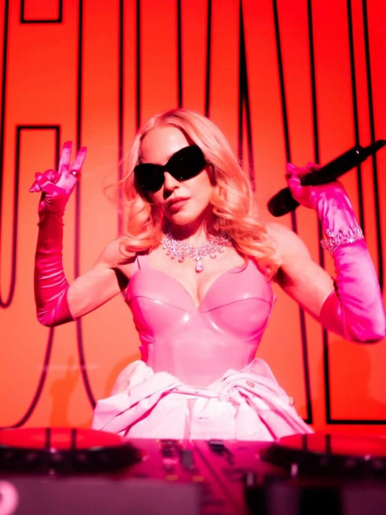 Madonna en un escenario con un micrófono, luciendo un atuendo rosa y gafas oscuras, celebrando el éxito de su álbum Confessions II.