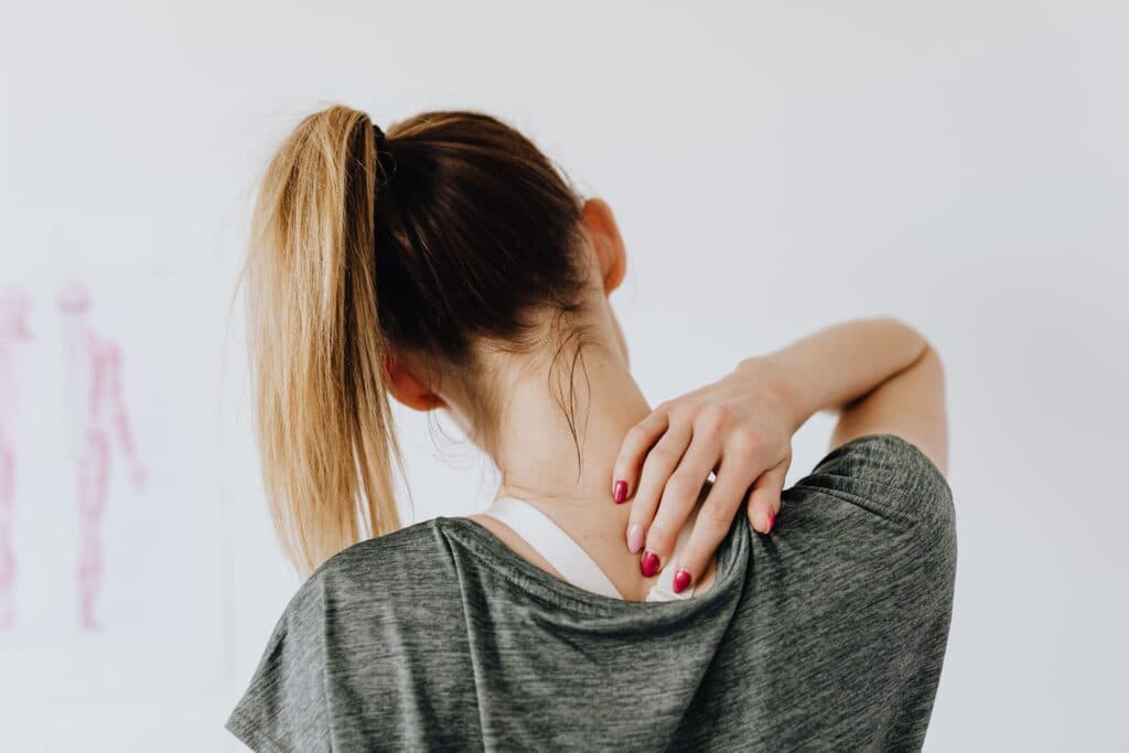 Mujer con cabello recogido se toca el cuello, mostrando signos de tensión muscular, reflejando el impacto de una mala postura.