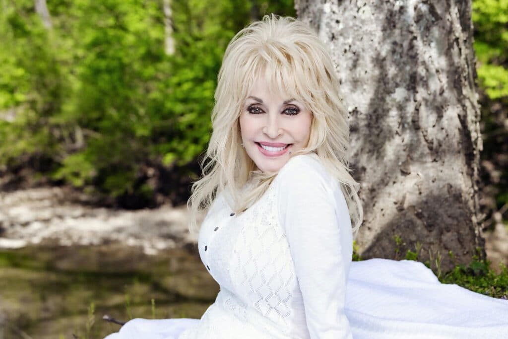 Dolly Parton sonríe en un entorno natural, recordada como una influyente figura de la música country y la filantropía.