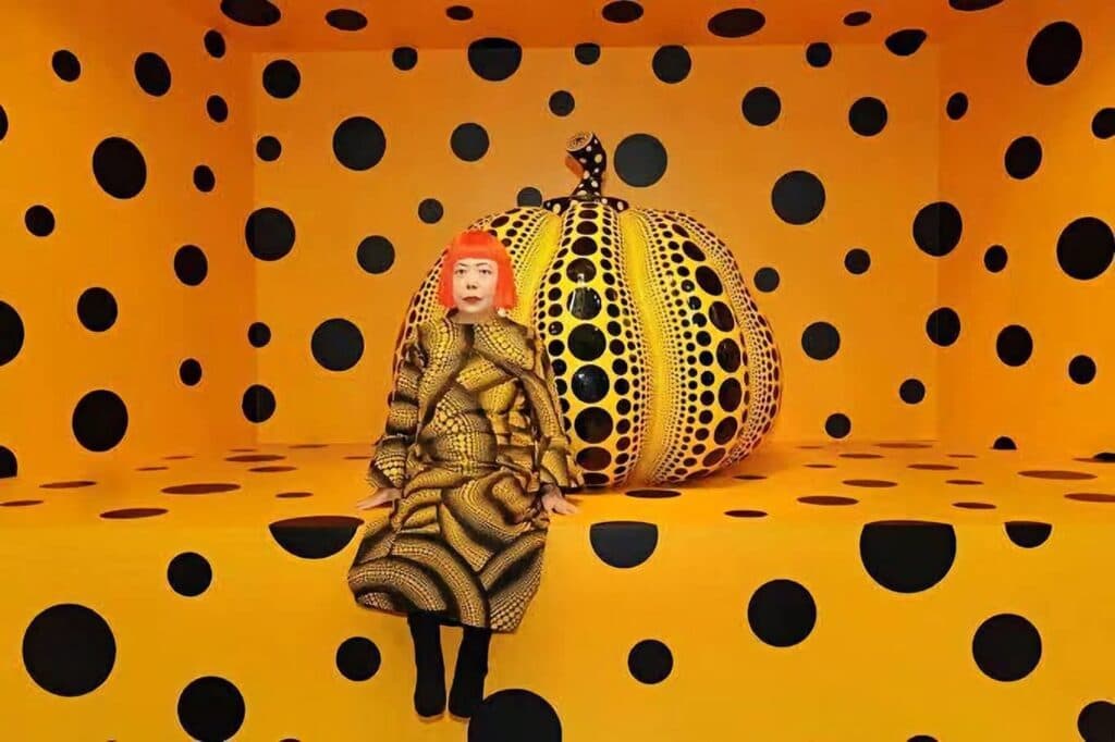 Yayoi Kusama en su icónica instalación de calabazas y lunares, reflejando su estilo único en el arte contemporáneo.
