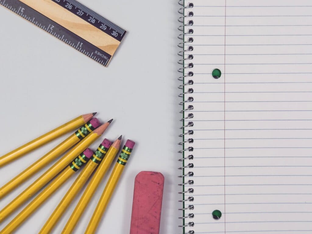 Útiles escolares como lápices amarillos, una regla y un cuaderno en un fondo blanco, reflejando la temporada de regreso a clases.