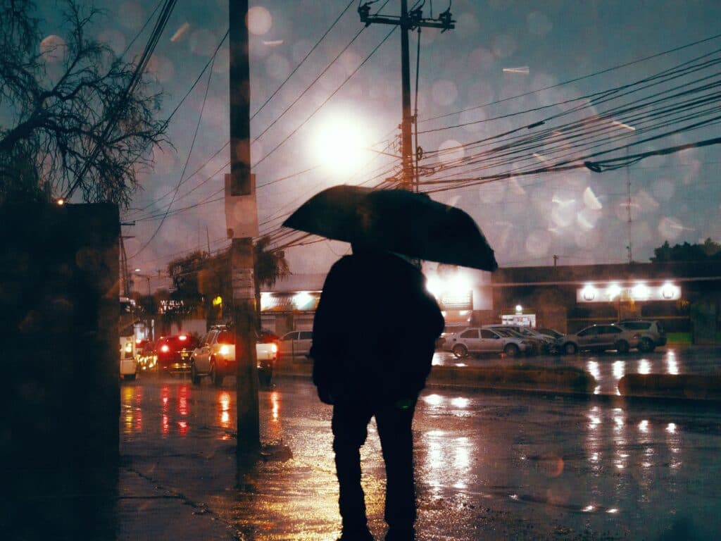 Persona con paraguas en una calle de la CDMX, bajo lluvia intensa y tormenta eléctrica, con luces de vehículos al fondo.