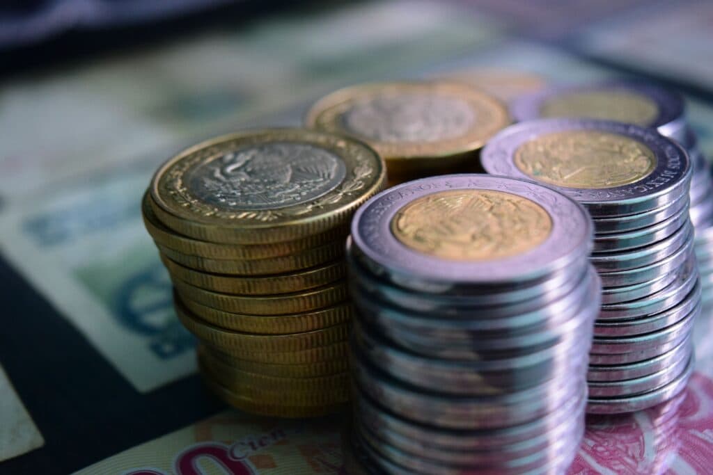 Monedas y billetes mexicanos apilados sobre una superficie, simbolizando la economía y la inflación en México.