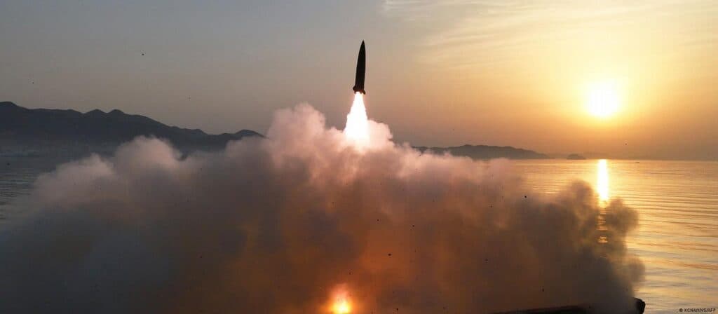 Lanzamiento de un misil balístico desde la costa de Corea del Norte al amanecer, con humo y llamas en el fondo.