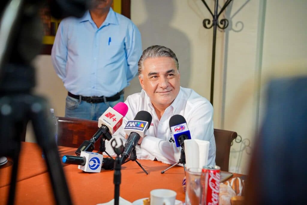 Jesús Ruiz Uribe sonríe durante una conferencia de prensa en Tijuana, rodeado de micrófonos y medios de comunicación.