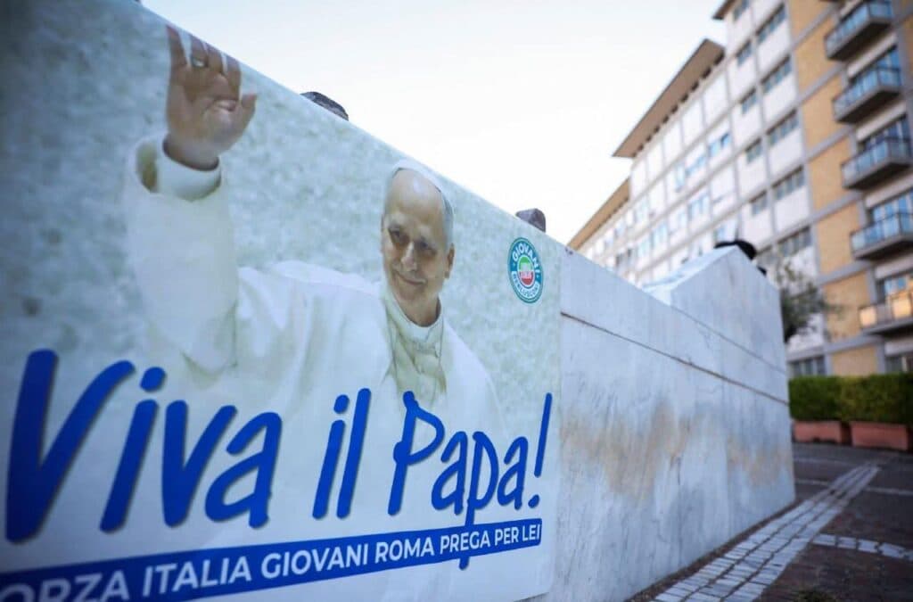 Pancarta con la imagen del papa León XIV y el mensaje "Viva il Papa!" en un entorno urbano, en apoyo a su salud.