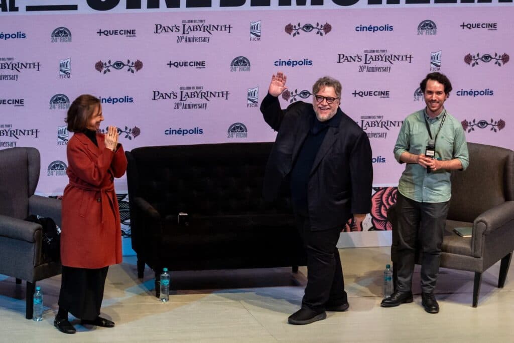 Guillermo del Toro saluda al público en el Festival Internacional de Cine de Morelia, mientras dos personas lo aplauden.