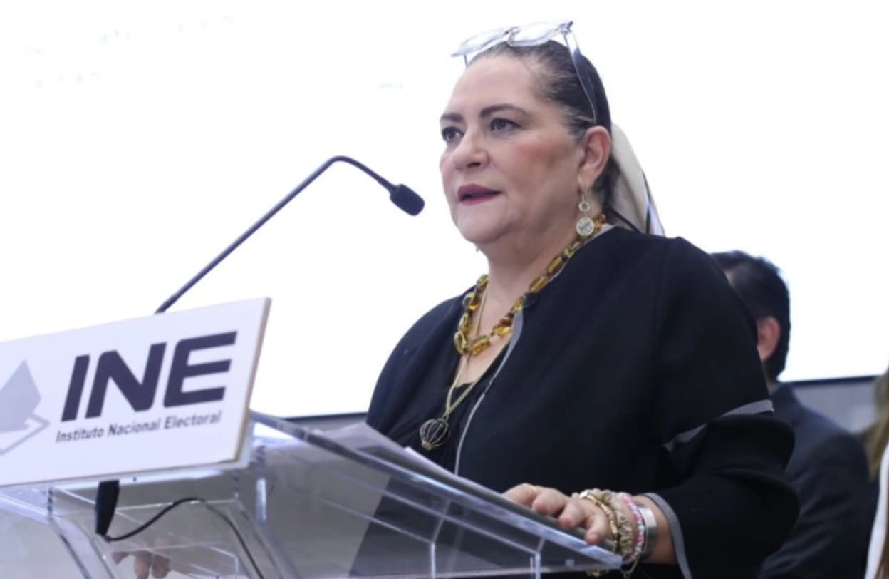 Funcionaria del INE en conferencia, con micrófono y fondo institucional, discutiendo temas electorales.