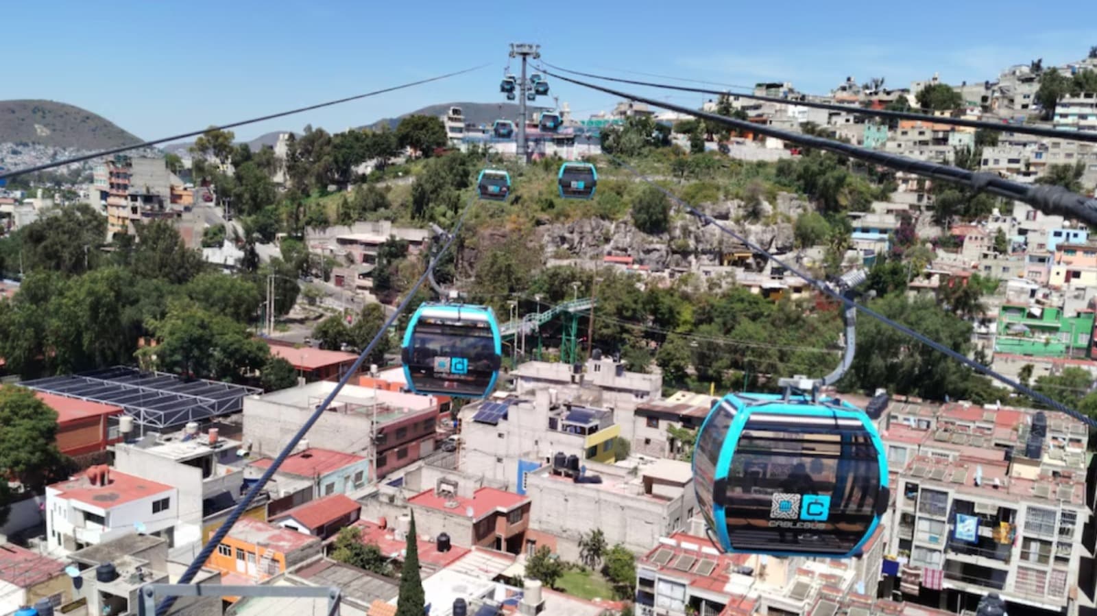 Vista panorámica de la Línea 5 del Cablebús en Álvaro Obregón, con cabinas suspendidas sobre casas y vegetación.