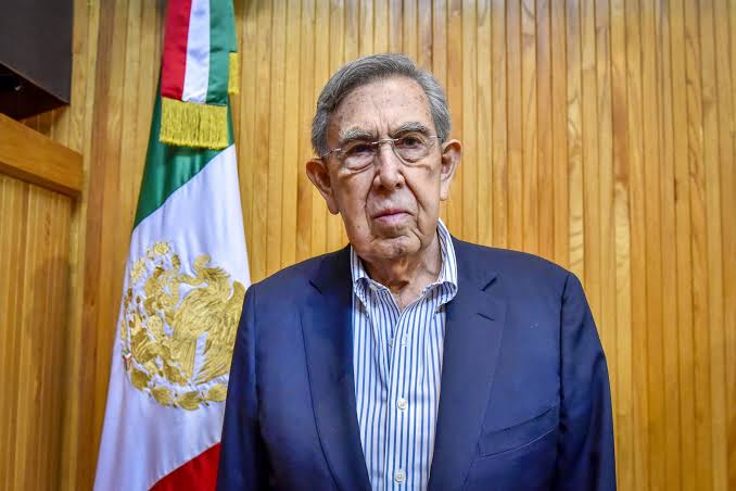 Cuauhtémoc Cárdenas, figura emblemática de la izquierda mexicana, posando frente a la bandera de México en un evento político.