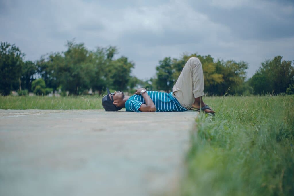 Hombre descansando en un parque, recostado sobre el césped, disfrutando de un domingo de desconexión y relajación.