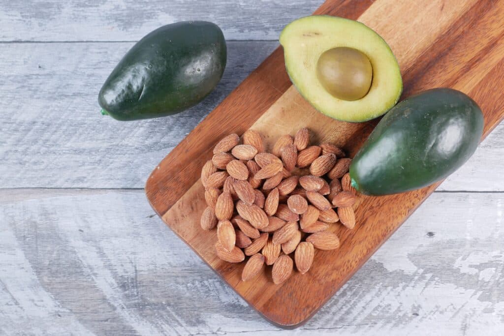 Aguacates y almendras sobre una tabla de madera, destacando fuentes vegetales de omega 3 para la salud.